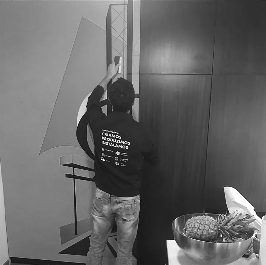 Técnico da MundoPinguim com t-shirt Criamos, Produzimos, Instalamos a aplicar vinil numa porta